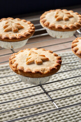 Homemade mince pies freshly baked on a stainless steel cooling rack. Christmas festive cooking concept.