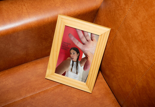 PSD mockup of  Wooden Photo Frame Resting on a Brown Leather Sofa in a Cozy Indoor Setting
