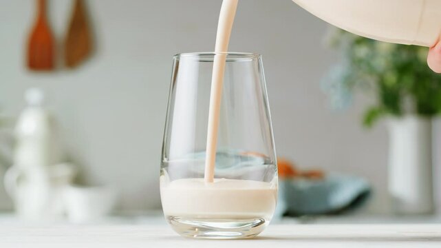 Pouring kefir yogurt into glass cup close-up. Glass with kefir or milk, lactic acid product dairy products concept. Drinking fresh lactose free in morning.