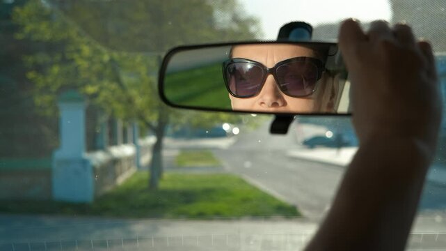 Adjusting mirror manually in car. A view of lady driver adjusting the mirror in the car in the sunny street.