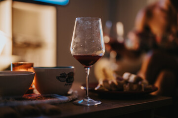 A warm, cozy setting featuring a glass of red wine on a table surrounded by appetizers. The atmosphere conveys relaxation and intimate conversation in a dimly lit room.