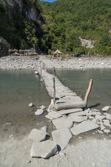 Osumi, Albania - August 15 2024: Handmade rustic wooden bridge (Ura e Vjeter e Zaberzanit) crossing the Osumi River on hot summer day, showcasing traditional Albanian craftsmanship and natural beauty