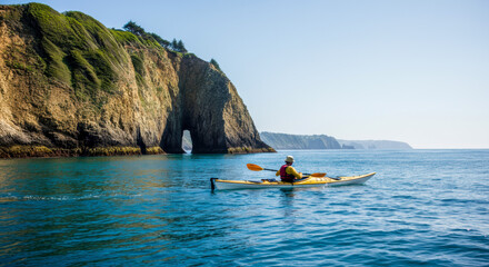 A kayaker explores the stunning cliffs and arch rock formations along the tranquil coastline on a sunny afternoon