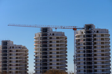 Fototapeta premium New residential towers under construction with cranes against a clear blue sky in a vibrant urban setting