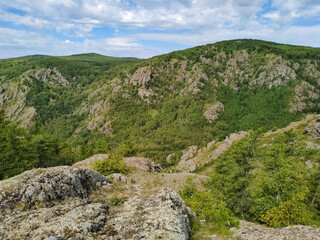 A majestic mountain, with vibrant trees and rugged surfaces, contrasts beautifully against a clear blue sky with fluffy clouds, creating a serene and inspiring natural scene