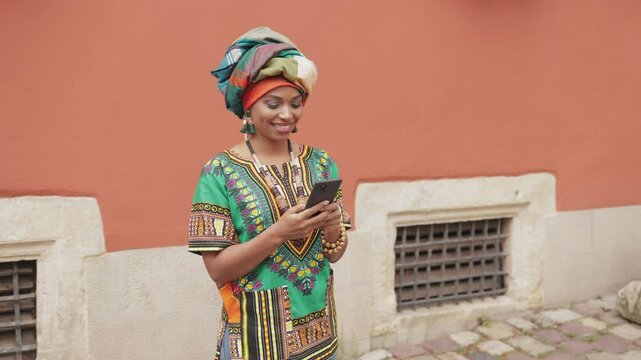 Camera sliding away from beautiful African American female. Woman standing still while using mobile device. Typing something on screen while smiling from joy. Concept of modern communication.