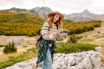 Naklejka premium Female trekker studying a map. Young woman hiking in autumn landscape with a map. Travel, nature concept