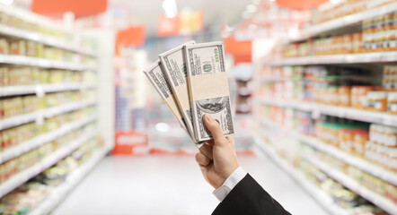 Male hand holding stacks of money in a supermarket
