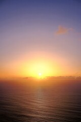 Maderia - A tranquil sunset over the ocean, with the sun gradually disappearing below the horizon, casting warm golden hues across the sky and reflecting on the calm water.