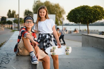 Cute kids in stylish casual clothes in skate park. They ride on skates and scooters. Summer vacation