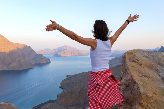 woman admires the panoramic view of the Musandam fjords from a rocky cliff at sunset, Khor Najd, Oman