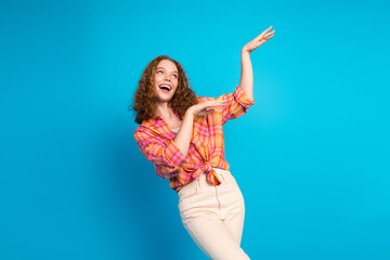 Joyful young woman in casual attire gesturing happily against a bright blue background