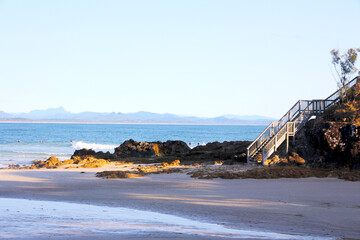 Wooden stairs leading to empty sandy beach lit by the sun in Byron Bay, Australia 
