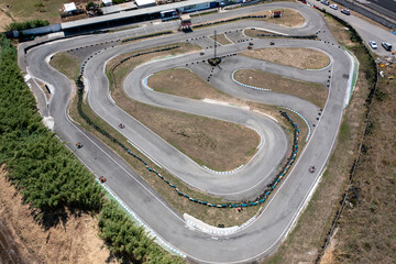 Drone capturing go-karts moving on winding race tracks from top aerial perspective. Distant view of racing competition on road at countryside during daytime. 