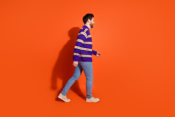 Fototapeta premium Young man in a striped sweater walking confidently on vibrant orange background showcasing casual style and movement