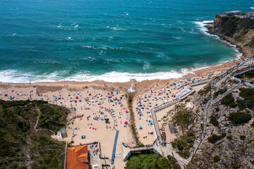 Naklejka premium Overhead drone view of anonymous people and parasols on sandy seashore at Magoito Beach. From above of famous destination in Sintra, Portugal during summer. 