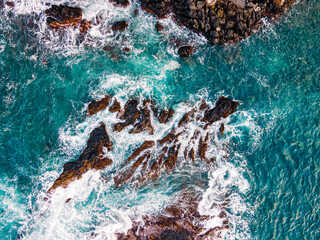 Aerial view of Turquoise waves crash against rocky coastline