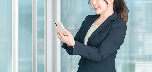 オフィスビルでスマホを使うビジネスウーマン（アプリ・動画視聴・SNS・音楽・検索・ニュース）
