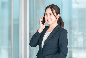 オフィス街でスマホで通話する若いアジア人ビジネスウーマン
