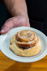 hand holds plate with cinnamon roll