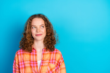 Fototapeta premium Young redhaired woman in casual plaid shirt posing with thoughtful and happy expression against bright blue background