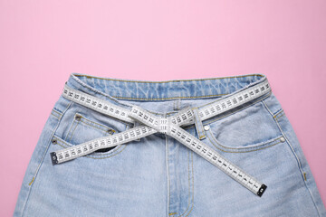 Jeans and measuring tape on pink background, top view