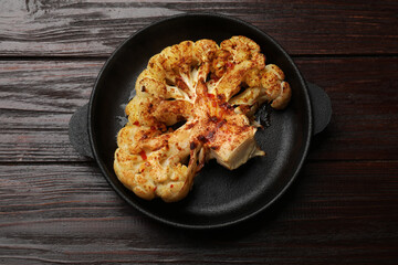 Tasty cauliflower steak in frying pan on wooden table, top view