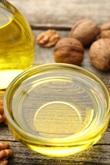Cooking oil in bowl and walnuts on wooden table, closeup