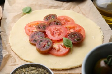 Raw galette with tomato and basil on wooden table, closeup