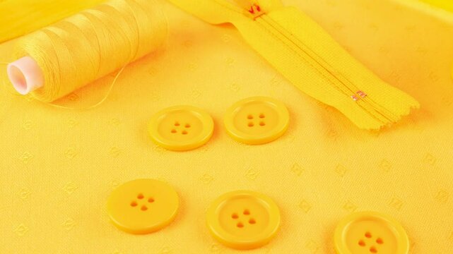 Cotton fabric and various sewing accessories in merigold yellow colors rotates on the showcase. Sewing zipper, buttons, threads, floss, yarn, satin ribbon. Background on the theme of sewing 