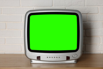 Retro Tv set with green screen on wooden table near white brick wall. Chroma key