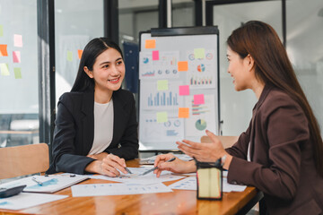 Professional women discussing business strategies in modern office. They are engaged in conversation, surrounded by charts and documents, showcasing teamwork and collaboration
