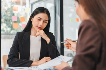 Professional women discussing business reports in office setting, showcasing focus and collaboration