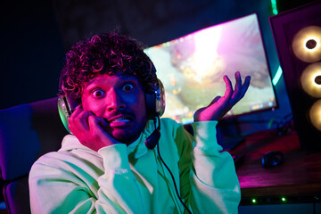 Photo of cute young guy scared panic bite nails play gamer computer purple blue neon light indoors late night