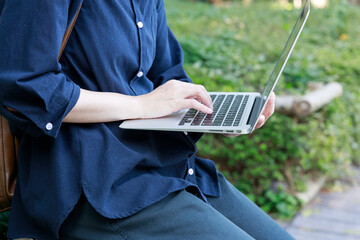 公園でノートパソコンを使用している女性　屋外　仕事　イメージ