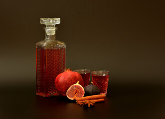 Fig-pomegranate liqueur in a crystal decanter and two glasses with spices on a black background,...