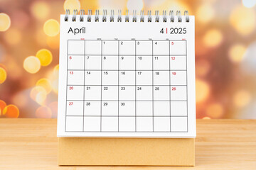 April 2025 desk calendar on wooden table with gold light bokeh.
