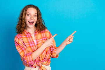 Excited young woman pointing with both hands against bright blue background, showcasing joyful expressions and casual style