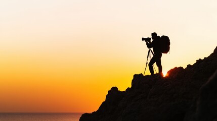 Fototapeta premium Silhouette of a photographer on a rocky hill capturing sunset. Perfect image for adventure, travel, and nature themes.