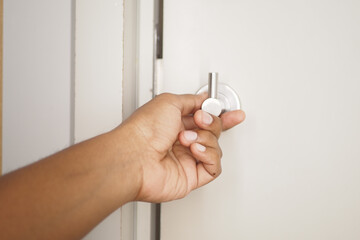 A hand is turning a door knob on a beautifully painted white door to gain entry inside