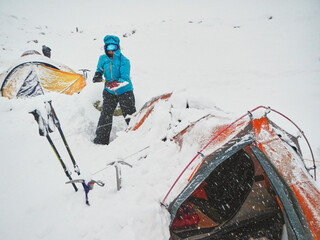 Woman mountaineer removes snow from above and around her tent during a snowfall using a shovel, in Mendoza, Argentina.