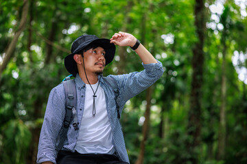 portrait of asian man sitting on a tree in rain forest looking up sky.