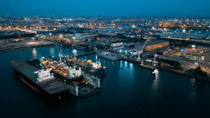 Fototapeta premium aerial view shipyard dry dock maintenance and repair container ship transport and oil ships in sea, business and industry heavy service at night over lighting cinematicphotography process