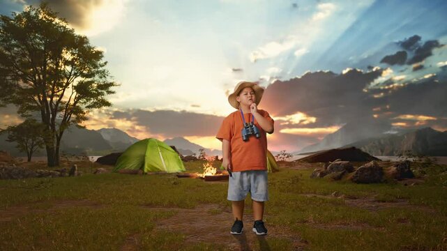 Asian Boy With A Hat, Binoculars Holding A Magnifying Glass, Thinking Then Raising His Index Finger While Tent Camp Lakeside. Boy Researcher, Travel Adventure, Full Body 