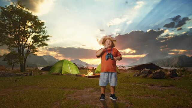 Asian Boy With A Hat Looking Through Binoculars Then Making Shh Gesture While Tent Camp Lakeside. Boy Researcher Examines Something, Travel Tourism Adventure Concept, Full Body