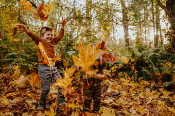 Little boys playing in the colorful fall leaves in the northwest.