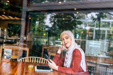 A thoughtful woman wearing a hijab sits in a cafe reflecting and enjoying the peaceful ambiance.