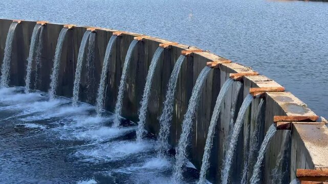 Close-up of a water flowing over concrete barrier. Row of thin trickles. Small river dam. Real time static video. 