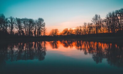 Fototapeta premium lake reflecting the colors of an evening sky, with silhouettes of trees in the background