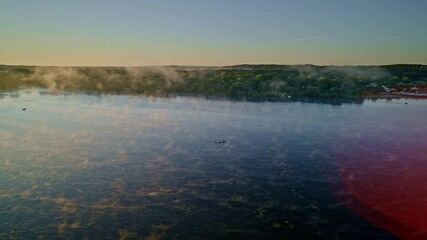 Peaceful drone shot of fishing boats on a foggy river at sunrise